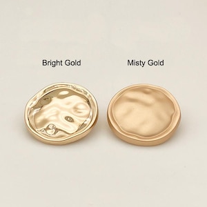 Pode incluir: Dois botões redondos dourados. Um é rotulado como "Bright Gold" e tem uma superfície texturizada e ondulada. O outro é rotulado como "Misty Gold" e tem um acabamento liso e fosco. Os botões são provavelmente para roupas ou projetos de artesanato.