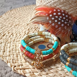 Può includere: Un set di quattro braccialetti colorati con perline e dettagli dorati. I braccialetti sono impilati uno sopra l'altro e presentano perline turchesi, rosse, marroni e bianche.