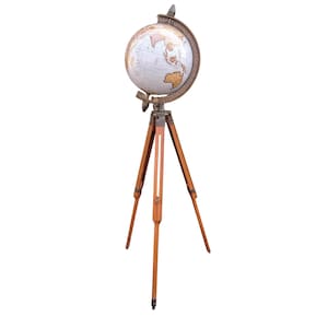 Puede incluir: Un globo terráqueo de estilo vintage sobre un trípode de madera. El globo presenta una superficie color crema con marcas geográficas detalladas y un anillo meridiano de color bronce. El trípode tiene tres patas de madera, lo que añade a la estética antigua.