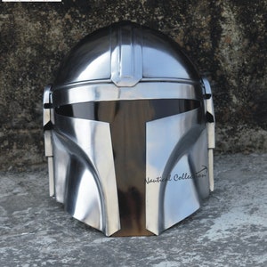 Könnte beinhalten: Ein silberner Mandalorianer-Helm mit schwarzem Visier. Der Helm ist aus Metall und hat ein detailliertes Design.