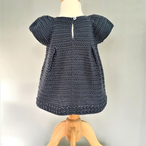 May include: A dark blue crocheted dress with short sleeves and a button closure in the back. The dress is displayed on a wooden mannequin.