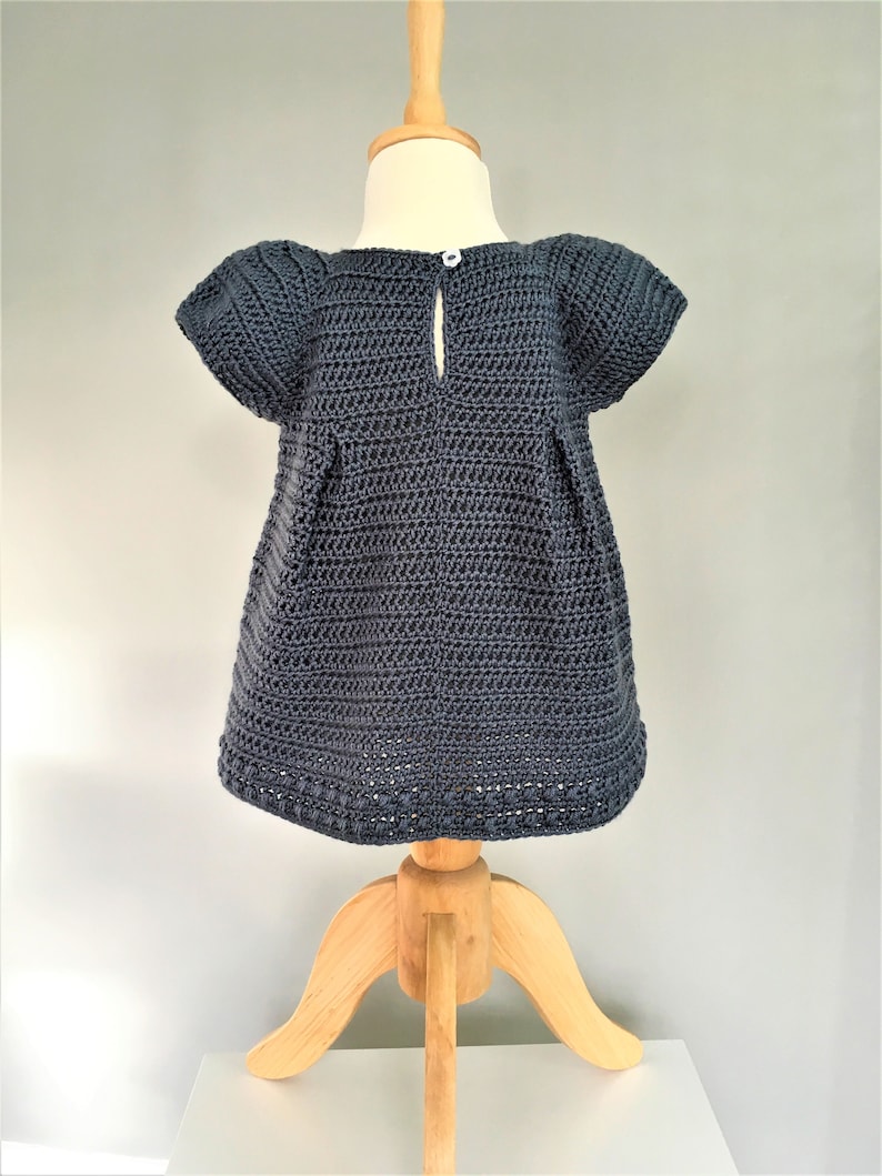 May include: A dark blue crocheted dress with short sleeves and a button closure in the back. The dress is displayed on a wooden mannequin.