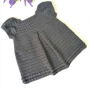 May include: A gray crocheted baby dress with short sleeves. The dress has a simple design and is made with a soft yarn.