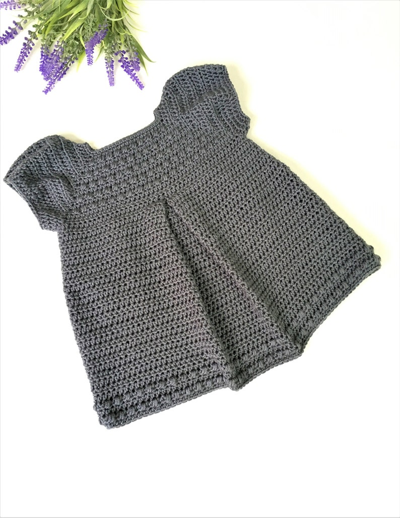 May include: A gray crocheted baby dress with short sleeves. The dress has a simple design and is made with a soft yarn.