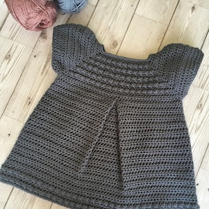May include: A gray crocheted baby dress with short sleeves and a scalloped hem.
