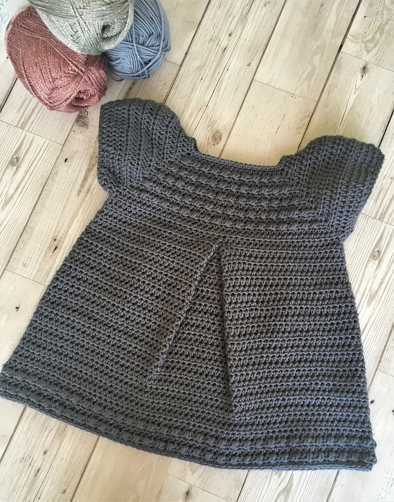 May include: A gray crocheted baby dress with short sleeves and a scalloped hem.