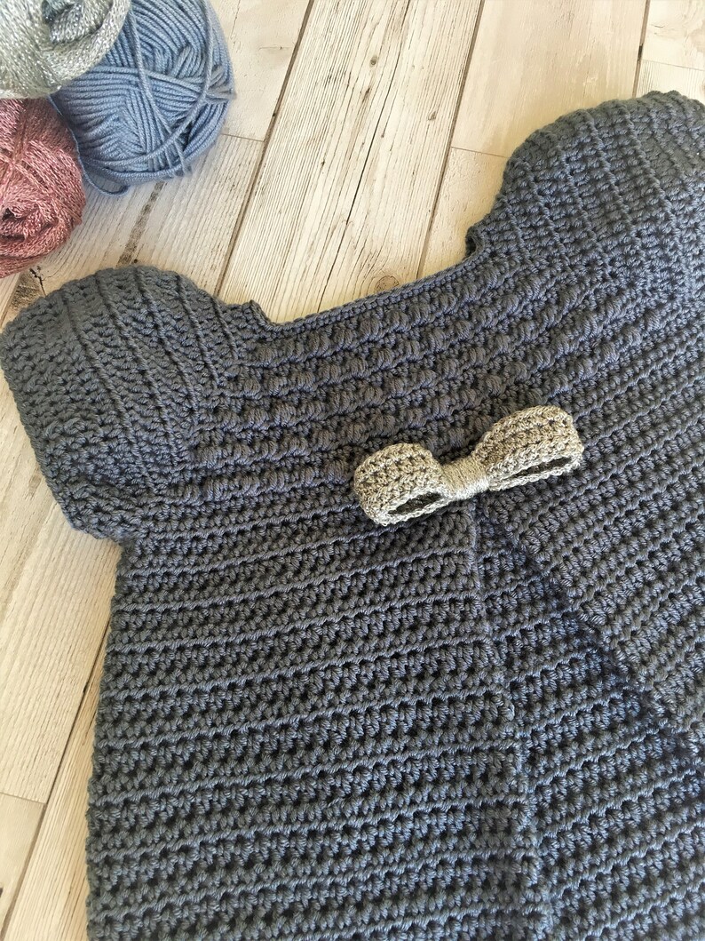 May include: A gray crocheted baby sweater with a gold bow on the front.