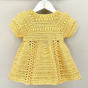 May include: A yellow crocheted baby dress with short sleeves and a flared skirt. The dress has a delicate crocheted pattern throughout.