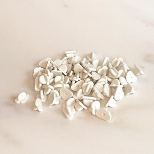 May include: A pile of white plastic pin back closures for making buttons or badges.