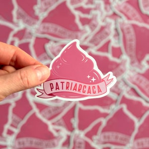 Peut inclure: Un autocollant rose avec un motif de crème fouettée et le texte "PATRIARCACA" sur une bannière. L'autocollant est tenu dans une main, avec un fond d'autocollants similaires.