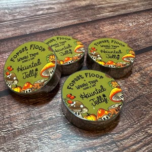 May include: Four rolls of washi tape with a forest theme. Each roll has a green label with the words "Forest Floor + Haunted Jelly" and illustrations of mushrooms and berries. The tape is 15mm x 10m.