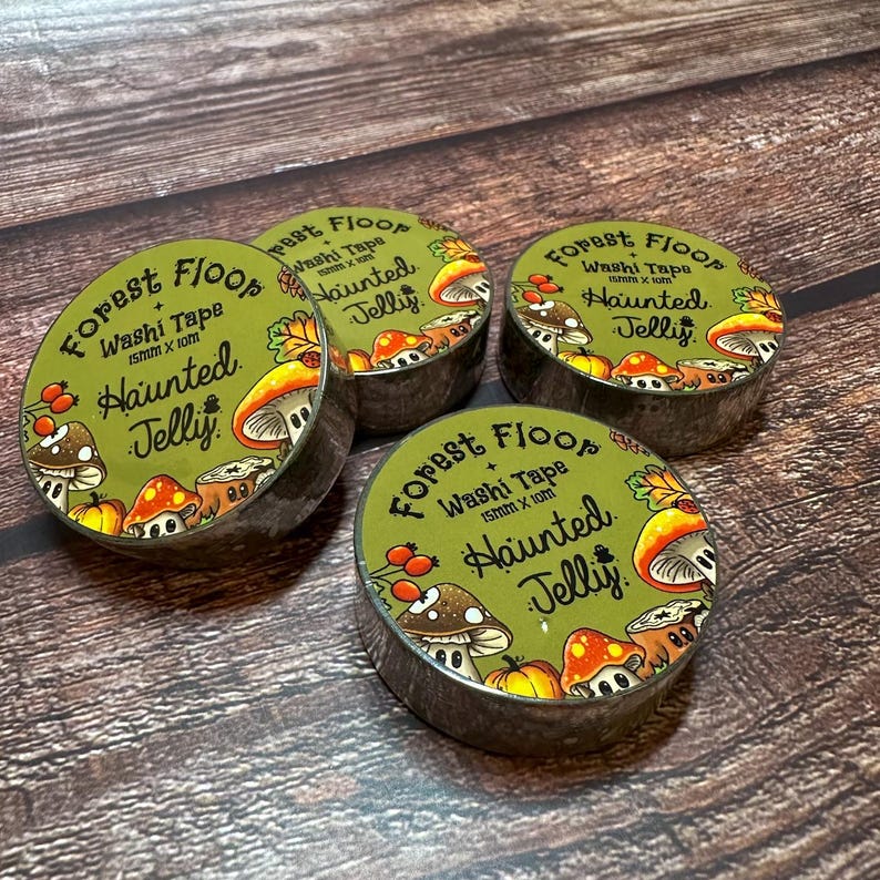 May include: Four rolls of washi tape with a forest theme. Each roll has a green label with the words "Forest Floor + Haunted Jelly" and illustrations of mushrooms and berries. The tape is 15mm x 10m.
