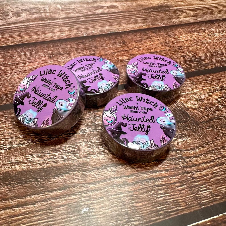 May include: Four rolls of washi tape with a purple background and the text "Lilac Witch Haunted Jelly." Each roll features illustrations of a witch hat, cauldron, and books. The tape is 15mm x 10m.