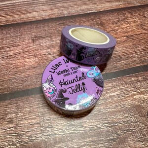 May include: Two rolls of washi tape with a Halloween theme. The tape is purple with illustrations of witch hats, potion bottles, and other spooky elements. The text "Lilac Washi Tape" and "Haunted Jelly" are visible.