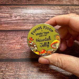 May include: A roll of washi tape with a forest theme. The tape is labeled "Forest Floor" and "Haunted Jelly" with illustrations of mushrooms, berries, and leaves. The tape is 15mm x 10m.