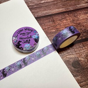 May include: A roll of purple washi tape with a Halloween theme. The tape features illustrations of witch hats, cauldrons, cats, and the text "Lilac Witch Haunted Jelly". The tape is 15mm x 10m.