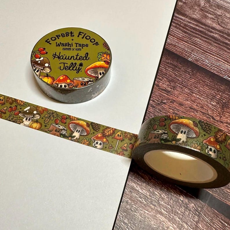 May include: Green washi tape with a repeating pattern of cartoon mushrooms, pumpkins, and leaves. The tape roll has the text "Forest Floor + Haunted Jelly". The tape is 15mm x 10m.