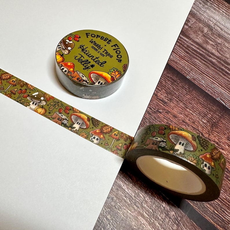 May include: A roll of washi tape with a forest-themed design featuring mushrooms, leaves, and the text "Forest Floor Haunted Jelly." The tape is olive green with a repeating pattern of cartoon illustrations.