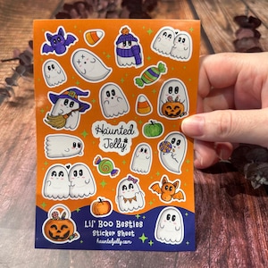 Puede incluir: Una hoja de pegatinas naranja con ilustraciones temáticas de Halloween. La hoja incluye fantasmas de dibujos animados, murciélagos, calabazas y caramelos. El texto en la hoja dice "Haunted Jelly" y "Lil' Boo Besties Sticker Sheet hauntedjelly.com".