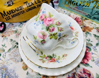May include: A white teacup and saucer set with a floral pattern featuring pink and blue flowers. The set has a gold trim around the edges.