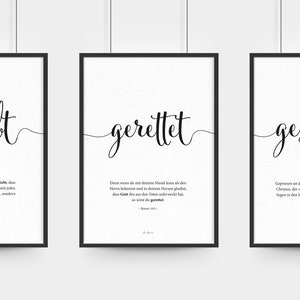 Könnte beinhalten: Drei schwarze gerahmte Drucke mit weißen Hintergründen und schwarzer Kalligraphie. Die Drucke zeigen die Wörter "geliebt", "gerettet" und "gesegnet" mit entsprechenden Bibelversen.