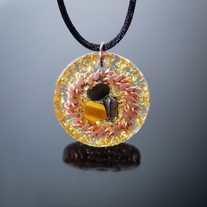 May include: A round gold and copper pendant necklace with a black cord. The pendant features clear resin with gold flakes, copper wire, and tiger's eye and black stones.