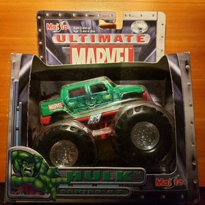 Op de afbeelding: Een groen en zwart monstertruck speelgoed met de woorden "Ultimate Marvel" en "Hulk" op de verpakking. De truck heeft een groene carrosserie met een Hulk-afbeelding en de woorden "Marvel" aan de zijkant. De truck staat op een zwarte en zilveren achtergrond.