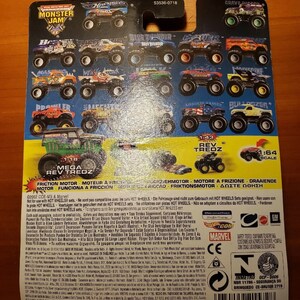 Op de afbeelding: Een close-up van de achterkant van een Monster Jam speelgoedautoverpakking. De verpakking is blauw, zwart en rood met afbeeldingen van verschillende Monster Jam trucks. De tekst op de verpakking luidt "Monster Jam", "Schaal 1:64", "Wrijvingsmotor", "Rev Tredz", "Mega Rev Tredz" en "53536-0718".