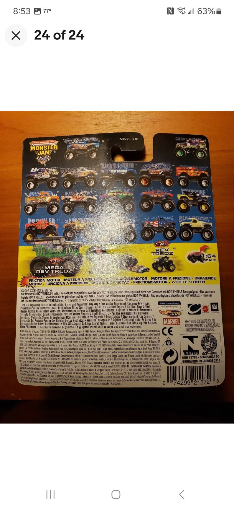 Op de afbeelding: Een close-up van de achterkant van een Monster Jam speelgoedautoverpakking. De verpakking is blauw, zwart en rood met afbeeldingen van verschillende Monster Jam trucks. De tekst op de verpakking luidt "Monster Jam", "Schaal 1:64", "Wrijvingsmotor", "Rev Tredz", "Mega Rev Tredz" en "53536-0718".