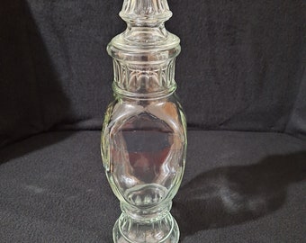 May include: A clear glass jar with a tall, pointed lid. The jar has a textured, fluted design and a rounded body. The lid is also textured and has a pointed top.