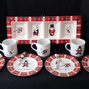Puede incluir: Un juego de vajilla navideña con tazas, platos y una fuente rectangular blancos. Los artículos presentan personajes de animales de dibujos animados con trajes festivos y un diseño de cuadros rojos y blancos. Los platos tienen texto.