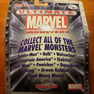 Op de afbeelding: Een zilveren en zwarte kartonnen doos met een zilveren metalen ontwerp. De doos heeft de tekst "Ultimate Marvel Monsters" en een lijst met Marvel-personages, waaronder Spider-Man, Hulk, Wolverine, Captain America, Elektra, Iron Man, Punisher, Daredevil, Thing en Green Goblin. De doos bevat ook de tekst "Motorized" en het Marvel-logo.