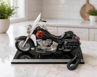 Pode incluir: Um telefone em forma de motocicleta preta e vermelha com detalhes cromados. O telefone tem um para-brisa transparente e uma base preta. O design inclui detalhes de chamas e um alforje.