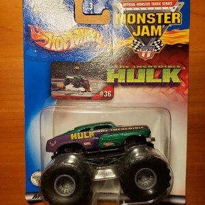 Op de afbeelding: Een groen en paars monstertruck-speelgoed met de woorden "The Incredible Hulk" aan de zijkant. Het speelgoed is verpakt in een blauwe en witte kartonnen doos met de woorden "Monster Jam" en "Hot Wheels" erop. Het speelgoed is nummer 36 in de serie.