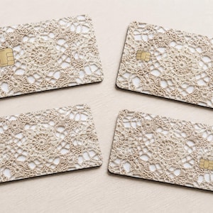 Pode incluir: Quatro cart&otilde;es retangulares com um padr&atilde;o de renda de croch&ecirc; bege. Cada cart&atilde;o tem um chip dourado no lado esquerdo. Os cart&otilde;es est&atilde;o dispostos em uma superf&iacute;cie bege clara.