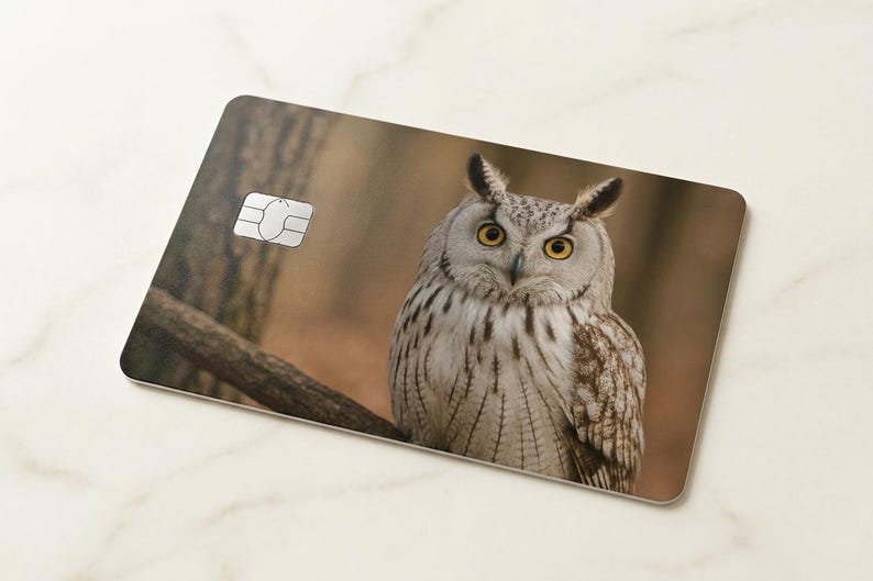 May include: A rectangular card featuring a detailed image of an owl with yellow eyes and a white and brown feathered body. The owl is perched on a branch against a blurred forest background. A silver chip is visible on the card.