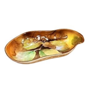 May include: A brown ceramic serving dish shaped like a peanut shell with a painted design of green leaves and brown nuts.
