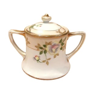 Może przedstawiać: Biała cukiernica z porcelany z pokrywką, ozdobiona złotą obwódką i kwiatowymi wzorami w odcieniach różowego, zielonego i brązowego.