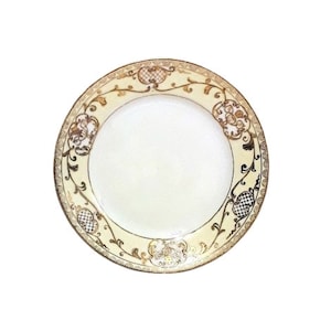 Può includere: Un piatto in ceramica bianca con un motivo floreale dorato e nero attorno al bordo.