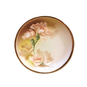 May include: A white porcelain bowl with a gold rim and a floral design featuring pink roses and green leaves.