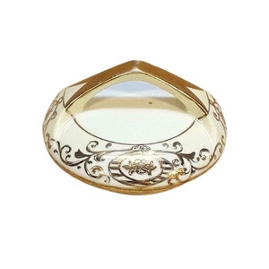 Może przedstawiać: Biała ceramiczna podstawka na pierścionki z pozłacanym rantem i misternymi wzorami kwiatowymi. Podstawka ma unikalny kształt z uniesionym uchwytem.