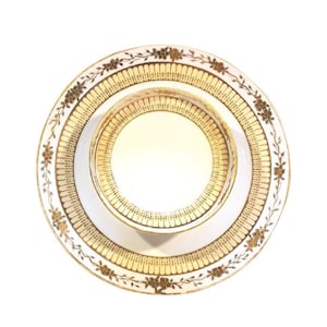 May include: A white porcelain saucer with a gold rim and floral design. The saucer has a matching teacup with a gold rim and floral design.
