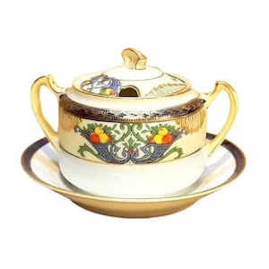 Puede incluir: Un azucarero de porcelana vintage con tapa, asas y platillo a juego. El cuenco y la tapa están decorados con ribetes dorados y un colorido diseño de cesta de frutas. El platillo tiene un borde dorado y un borde azul oscuro.