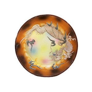 May include: A decorative ceramic plate with a raised, gold-colored dragon design. The plate has a brown rim and a white center with a multi-colored glaze.