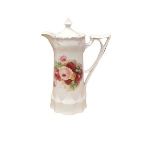 Puede incluir: Jarra de porcelana blanca con tapa, con un diseño floral de rosas rosas, rojas y amarillas con hojas verdes. La jarra tiene un asa decorativa y una superficie texturizada.