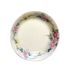 Może przedstawiać: Biała porcelana miska z kwiatowym wzorem. Miska ma jasnoniebieski i zielony brzeg z różowymi kwiatami.