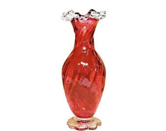 May include: A red glass vase with a ruffled top and a swirl design. The vase has a clear glass base.
