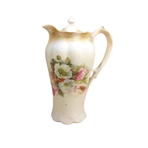 May include: A white porcelain creamer with a floral design. The creamer has a lid and a handle. The flowers are pink and white.
