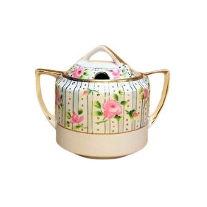 May include: A white porcelain sugar bowl with a lid, featuring a floral design of pink roses and green leaves on a blue and white striped background. The bowl has a gold trim and a small hole in the lid.