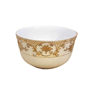 Puede incluir: Un tazón de cerámica blanca con un diseño floral dorado alrededor del borde. El tazón está vacío y tiene un acabado liso y brillante.